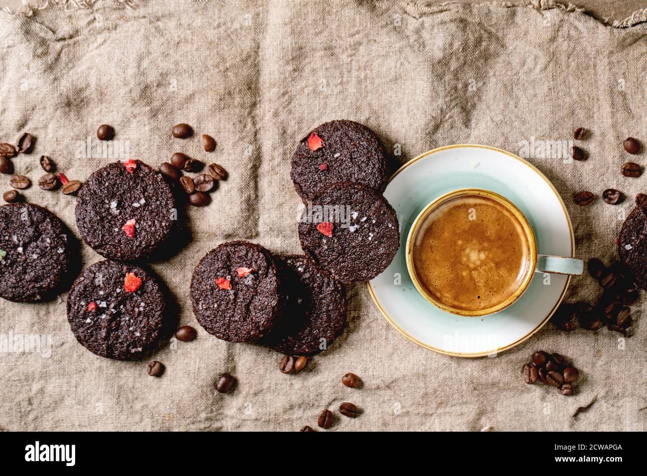 Biscotti salati al cioccolato fondente fatti in casa decorati da lamponi secchi, con scaglie di sale, chicchi di caffè, menta e tazza di caffè su panno di straccio Foto Stock