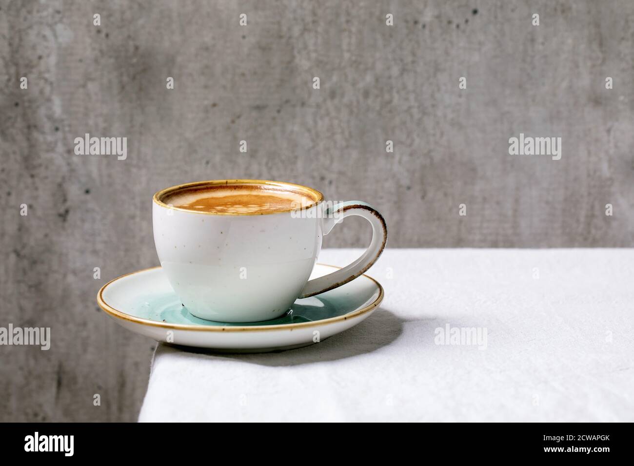 Caffè espresso nero con schiuma in tazza di ceramica bianca con piattino in piedi su tela da tavolo bianca in cotone. Spazio di copia Foto Stock