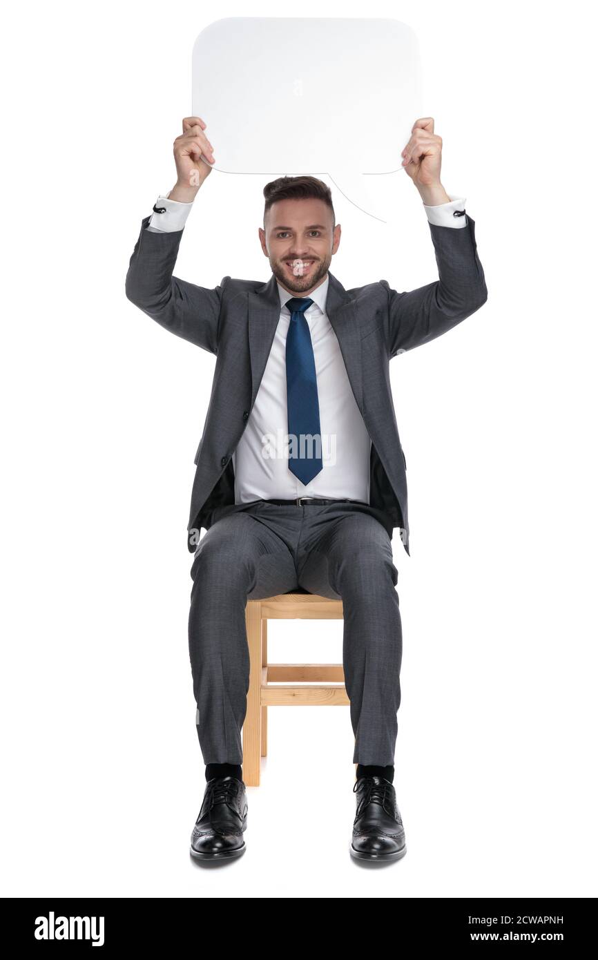 felice giovane uomo d'affari che tiene in su bolla di discorso e sorridente, seduto isolato su sfondo bianco, corpo pieno Foto Stock