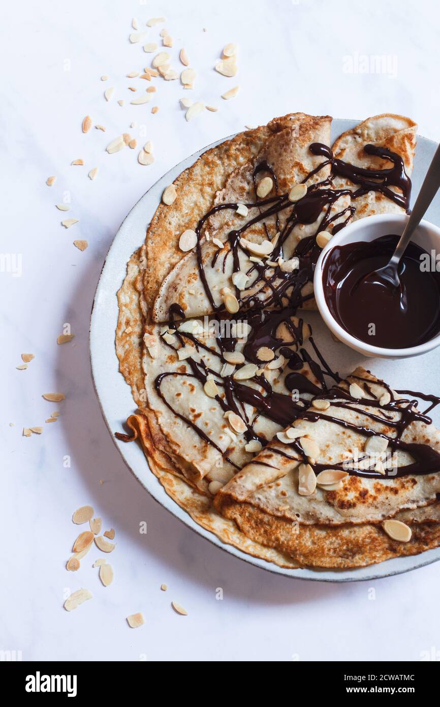 Impilare le crepes piegate su un piatto grande con un goccio di salsa al cioccolato fondente e mandorle tostate. Foto Stock