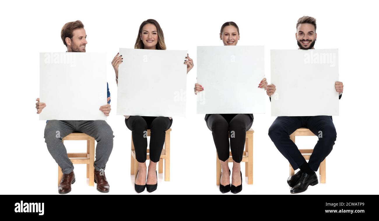 Squadra di 4 uomini d'affari felici che tengono i cartelloni vuoti mentre sedendo su sedie su sfondo bianco studio Foto Stock