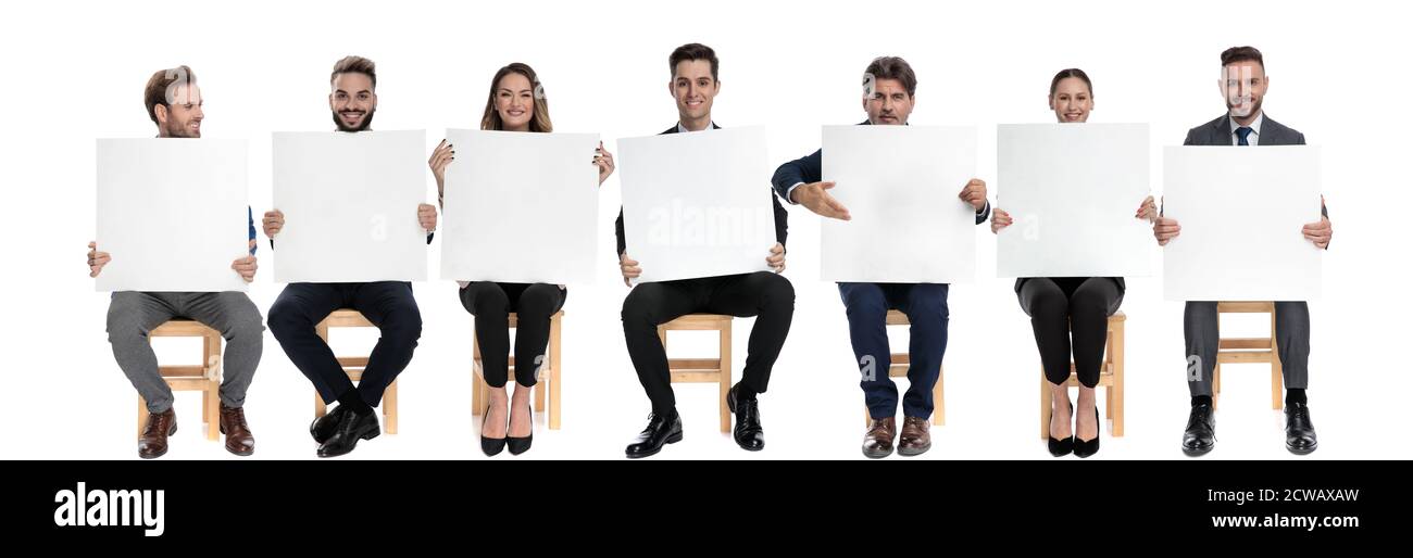 Squadra di 7 uomini d'affari che tengono i cartelloni vuoti mentre sta presentando il suo, seduto sulle sedie sullo sfondo bianco dello studio Foto Stock