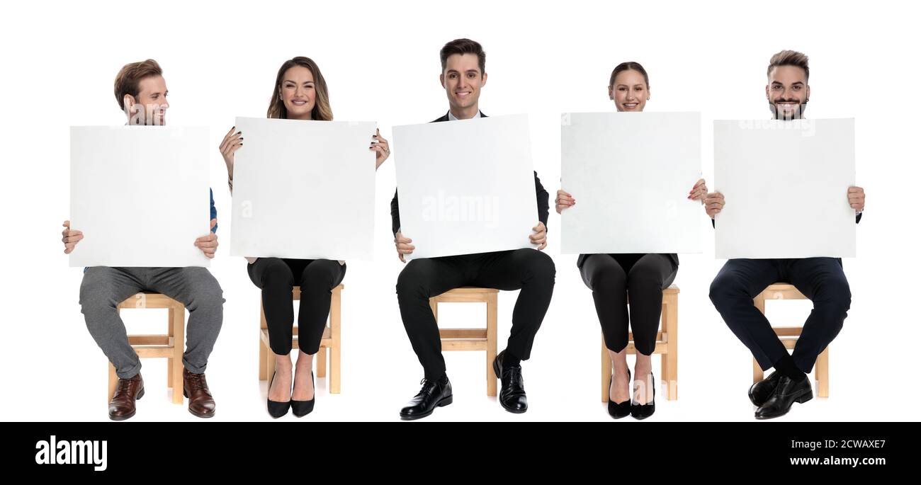 Squadra di 5 uomini d'affari felici che tengono i cartelloni vuoti mentre sedendo su sedie su sfondo bianco studio Foto Stock
