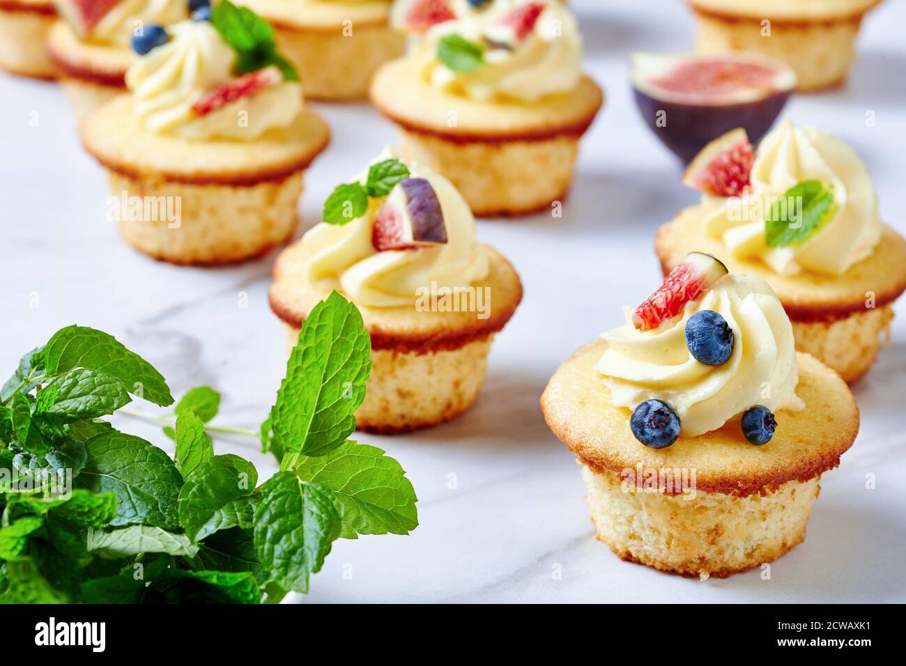 deliziosi cupcake con crema di burro e frutti di bosco freschi e menta su un tavolo di marmo, vista panoramica dall'alto, primo piano Foto Stock