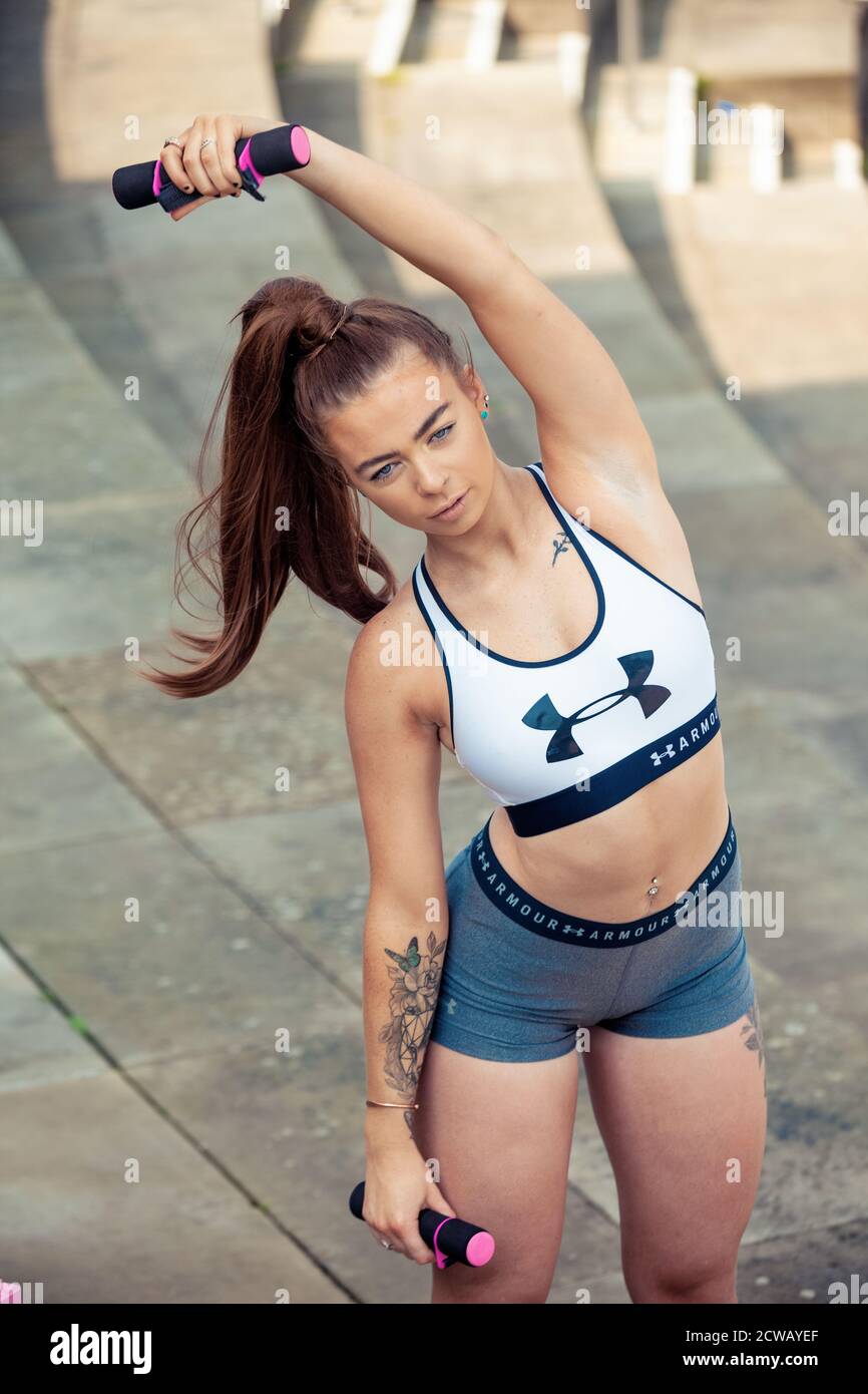 Una giovane donna che indossa abbigliamento sportivo e che usa pesi a mano per allungarsi. Foto Stock