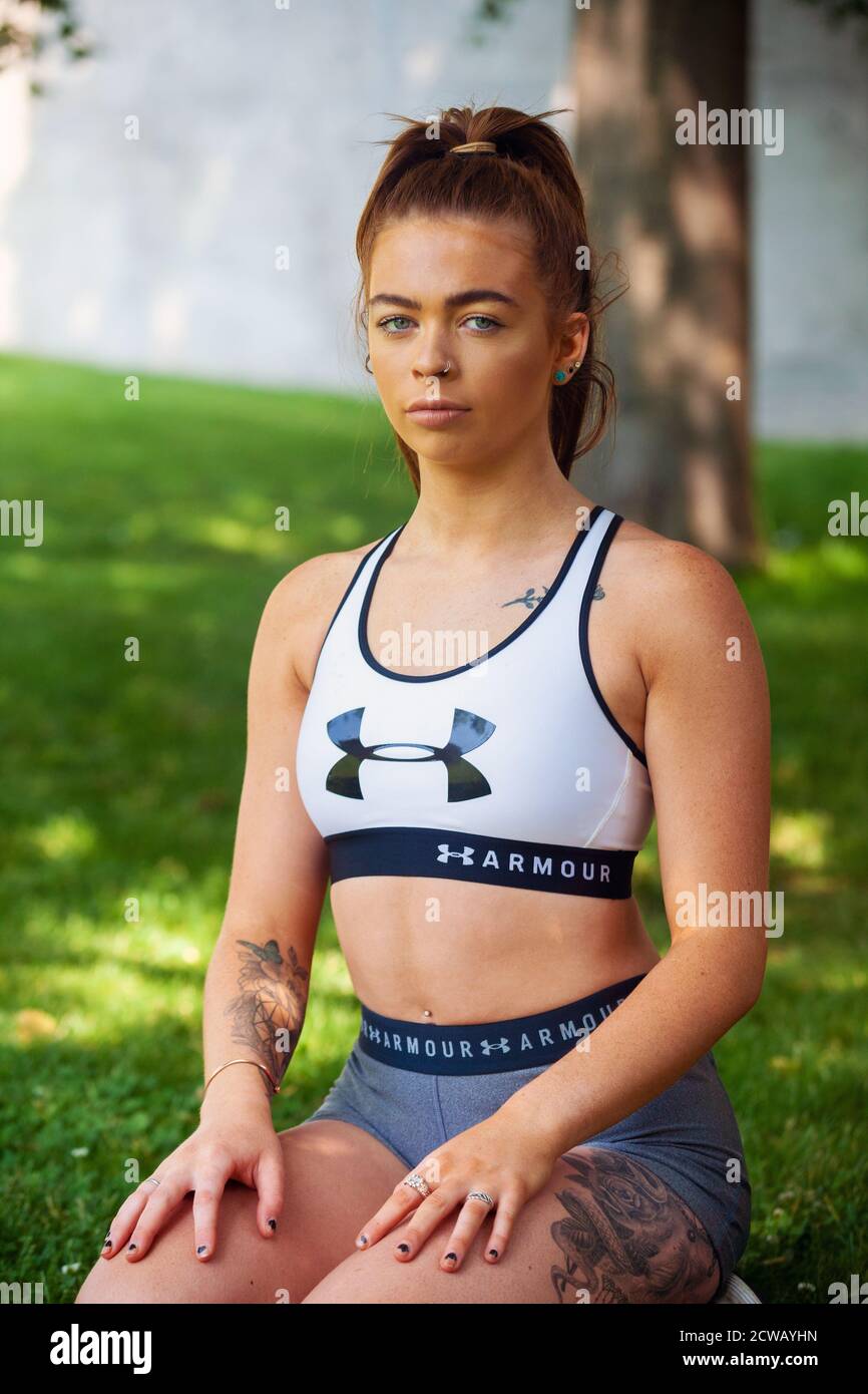 Una giovane donna che indossa abiti sportivi seduti all'ombra di un albero all'esterno. Foto Stock