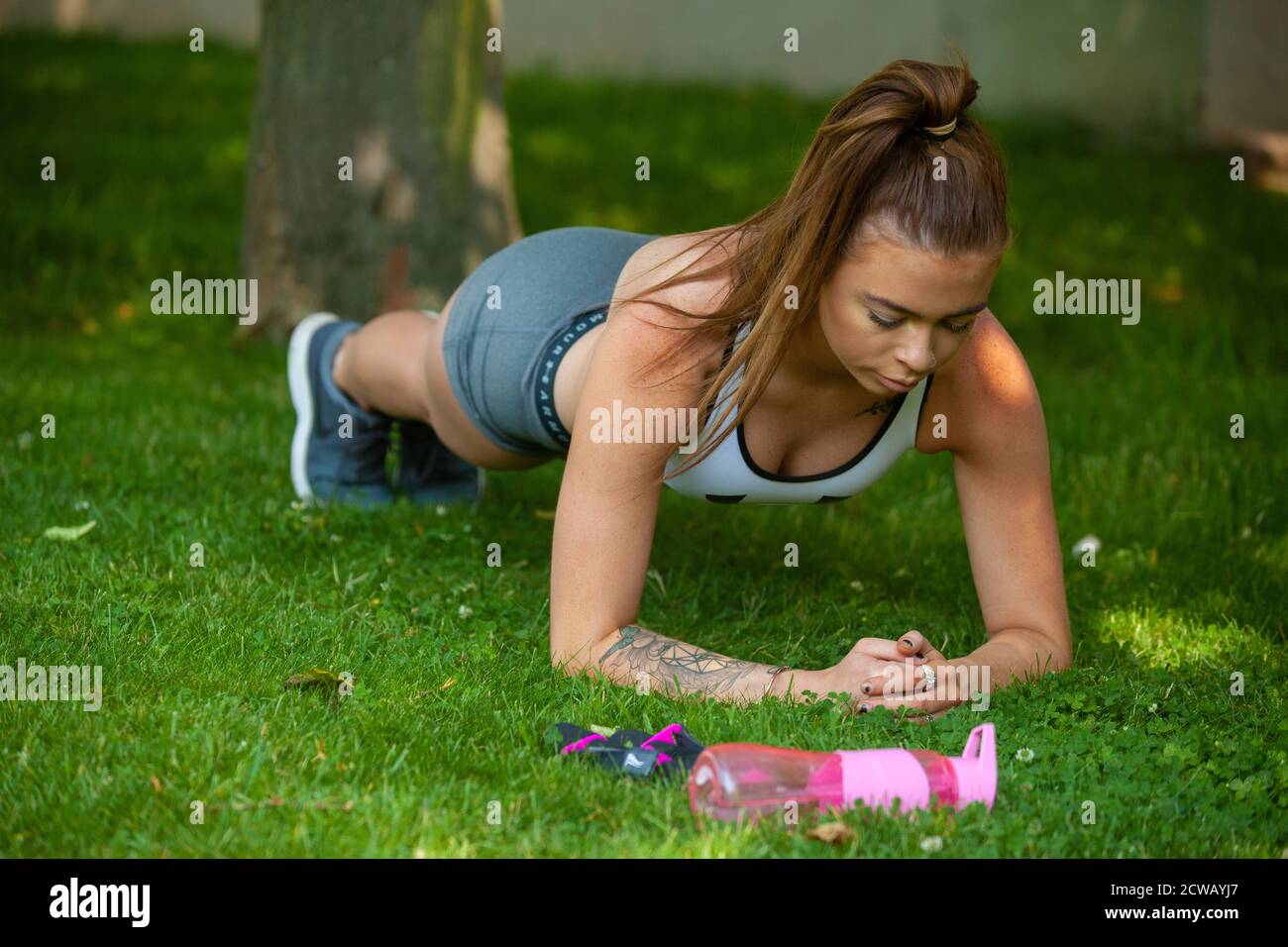 Una donna che indossa abbigliamento sportivo che esegue la posizione Plank all'esterno sull'erba. Foto Stock