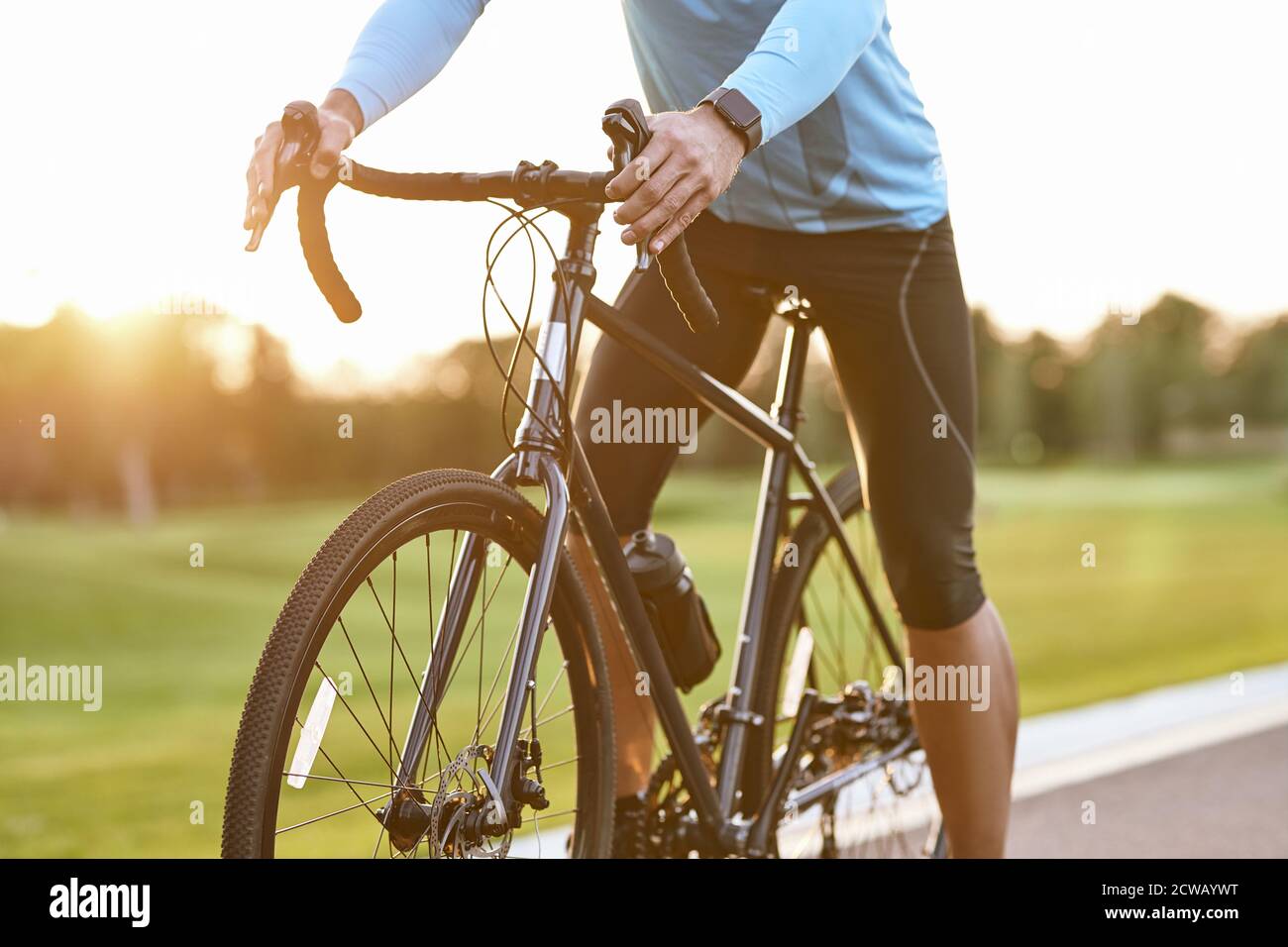 Tiro corto di professionista di corsa della bicicletta di strada in bici di sport che ciclano all'aperto al tramonto, uomo in piedi con la bicicletta sulla strada all'aperto. Stile di vita attivo e sport Foto Stock