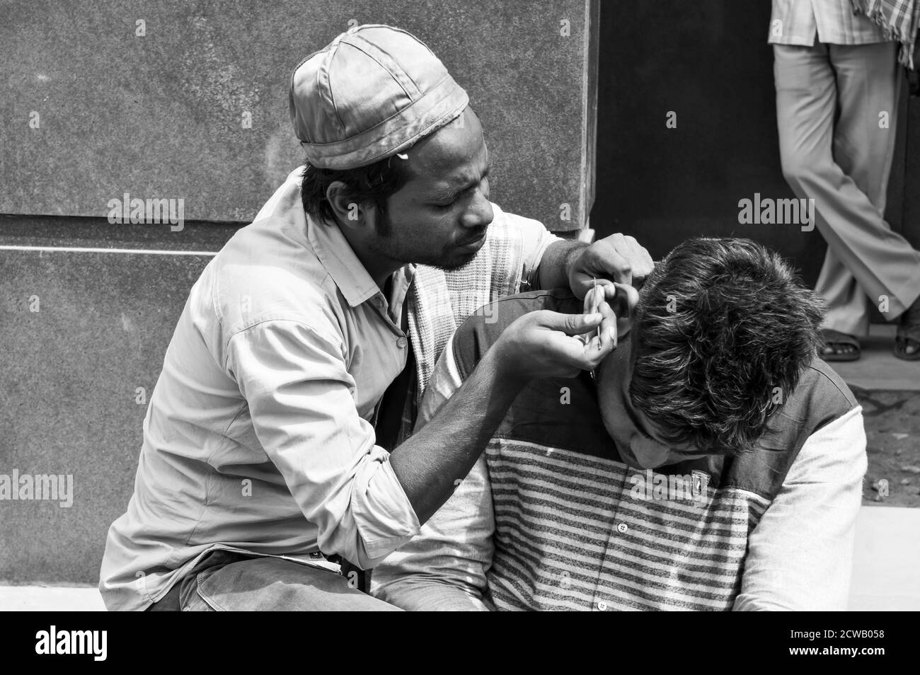 Un uomo sta pulendo l'orecchio del cliente, cera d'orecchi per soldi sulla strada trafficata in chandani chowk, vecchia delhi, india. Foto Stock