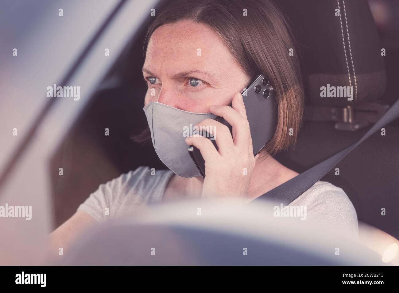 Donna con maschera protettiva che parla sul telefono cellulare l'auto durante le pandemie del coronavirus Foto Stock