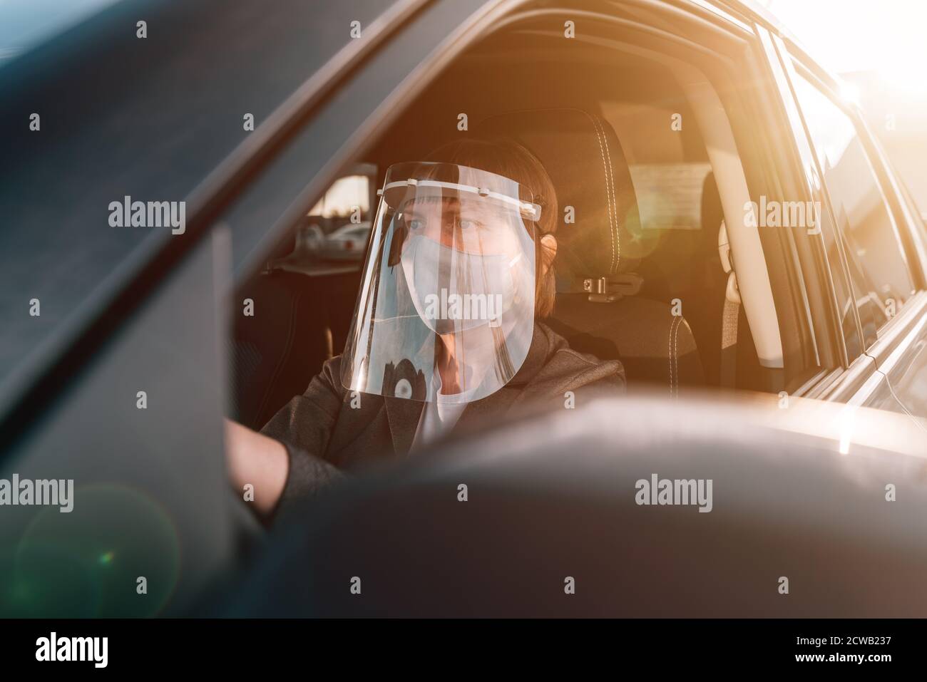 Tassista femmina con maschera protettiva e visiera in plastica in attesa in auto Foto Stock