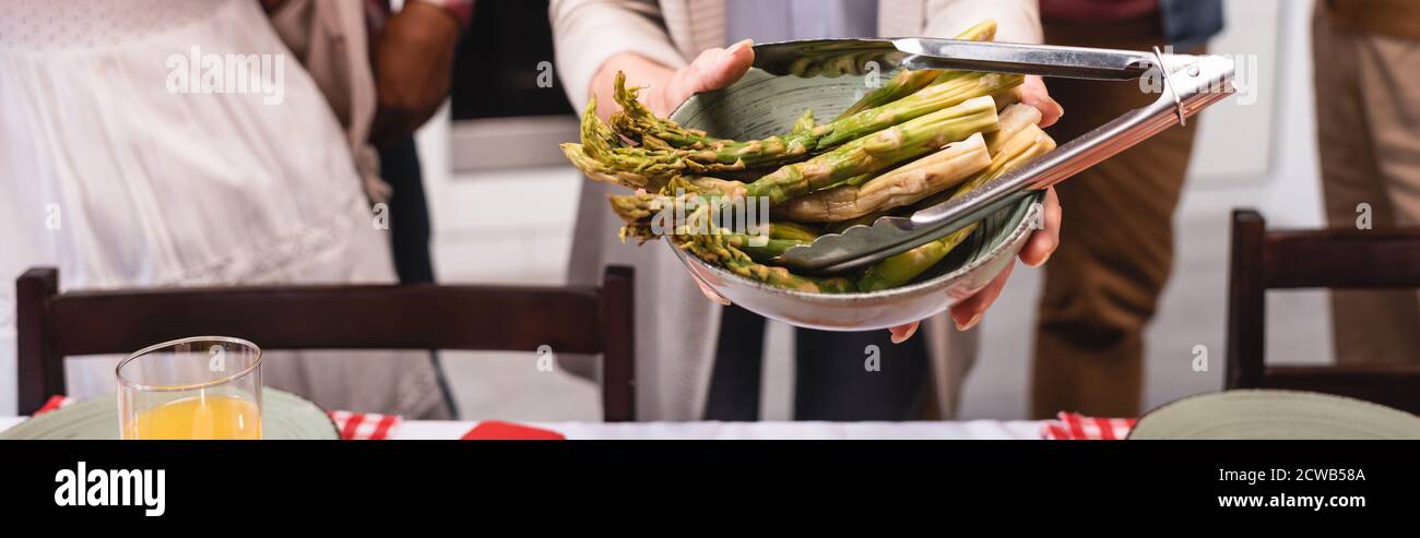 Immagine orizzontale di una donna anziana che tiene vicino la ciotola di asparagi famiglia multietnica durante il ringraziamento Foto Stock
