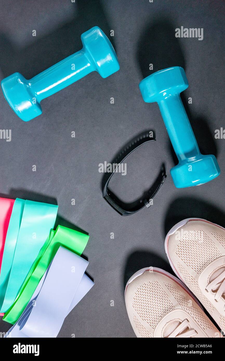 Concetto di fitness con sneakers, manubri, braccialetto fitness, tracker, espansori elastici. Attrezzature sportive su sfondo nero. Il concetto di healt Foto Stock
