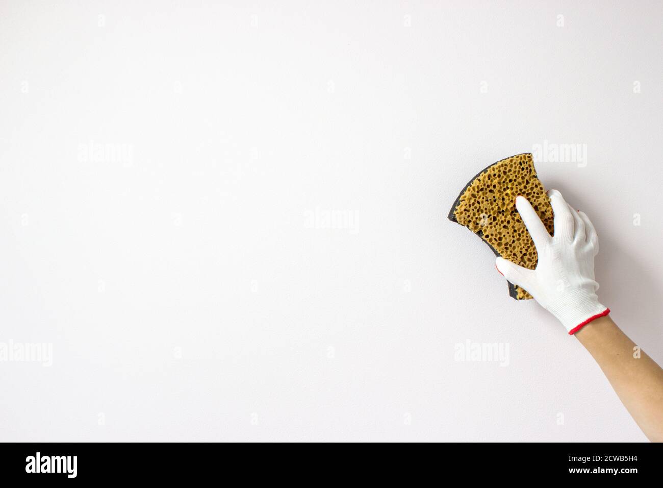 la mano tiene la spugna e lava un muro su uno sfondo bianco. Background del concetto di pulizia o pulizia Foto Stock