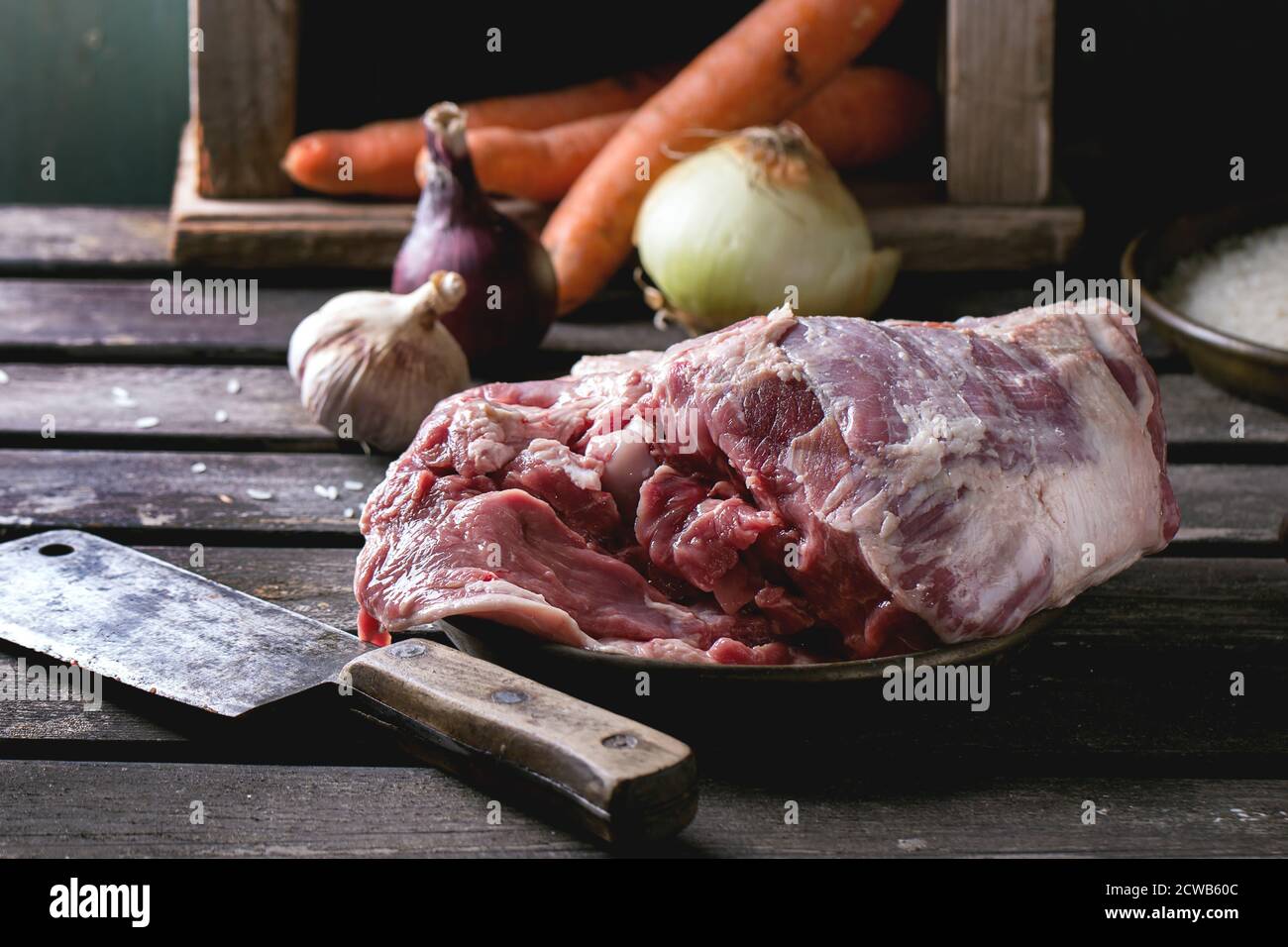 Ingredienti crudi per l'agnello pilaf, il riso, le carote, la cipolla e l'aglio con la spada di carne sopra il tavolo di legno. Stile rustico scuro. Foto Stock