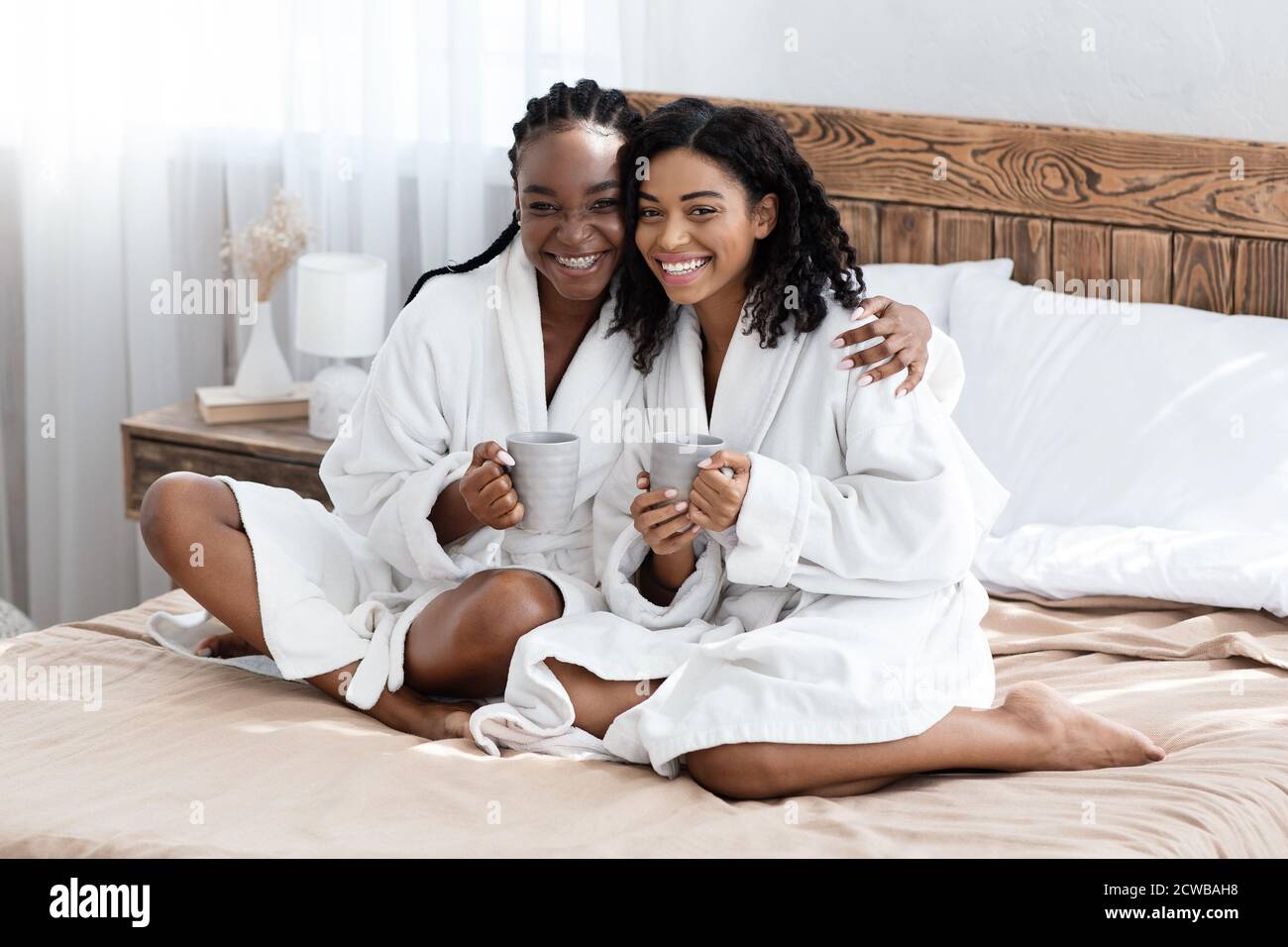 Assetati felici in accappatoi seduti sul letto, sorridendo alla macchina fotografica Foto Stock