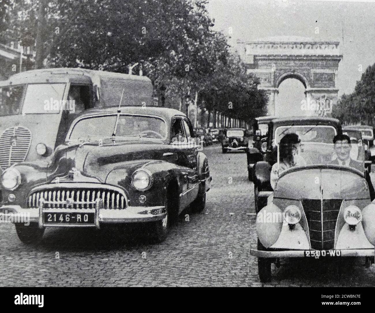 Fotografia in bianco e nero di immagini relative all'automobile alla metà del secolo; sulla Avenue Champs-Elysee un'automobile francese conosciuta come 'il bambino' vicino ad una Cadillac con l'Arco di Trionfo sullo sfondo. Foto Stock