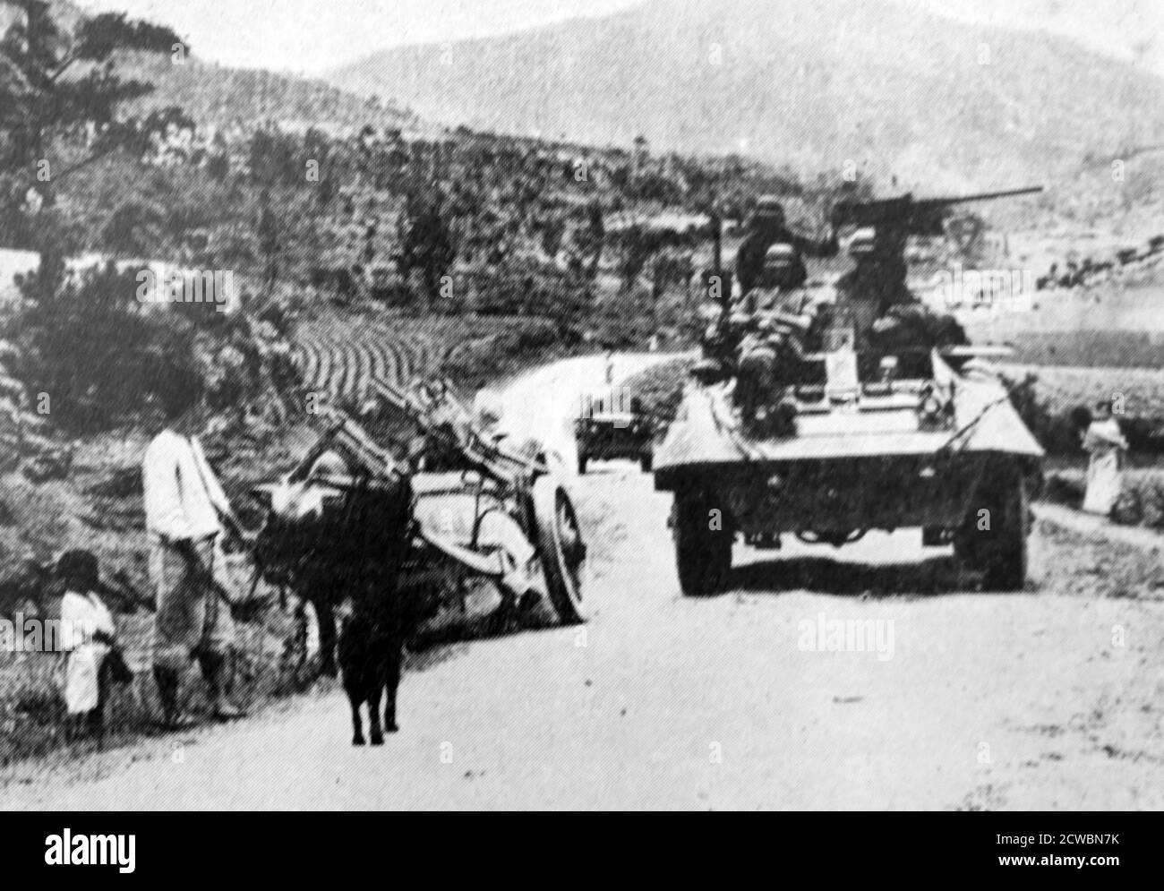 Fotografia in bianco e nero della guerra di Corea (1950-1953); un carro armato su una strada passa attraverso un trasporto trasportato da asino. Foto Stock