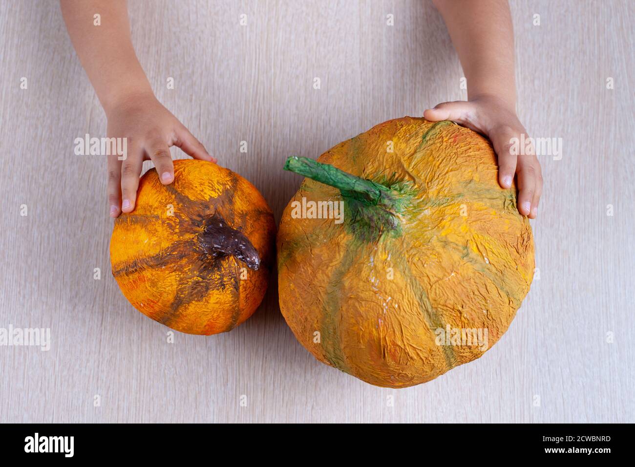 Le mani dei bambini tengono una zucca fatta in casa della papier-mache arancione per Halloween sul tavolo Foto Stock