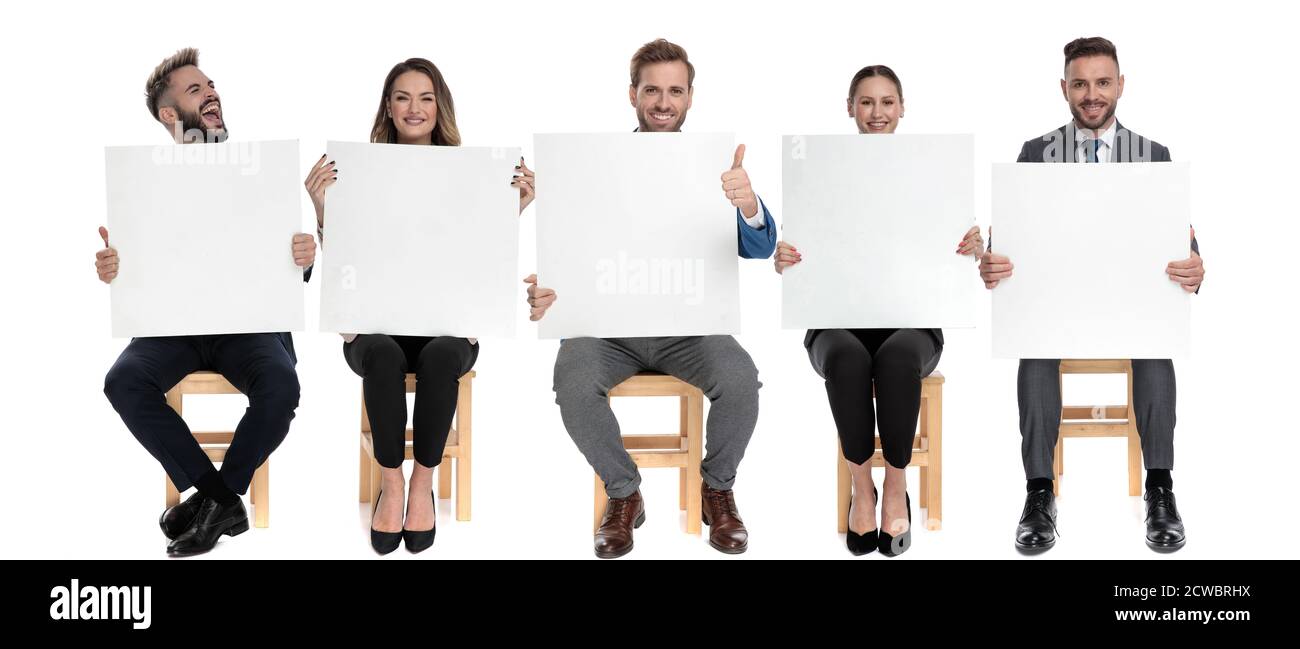 Squadra di 5 uomini d'affari che tengono i cartelloni vuoti e uno di gridano mentre si siedono sulle sedie sullo sfondo bianco dello studio Foto Stock
