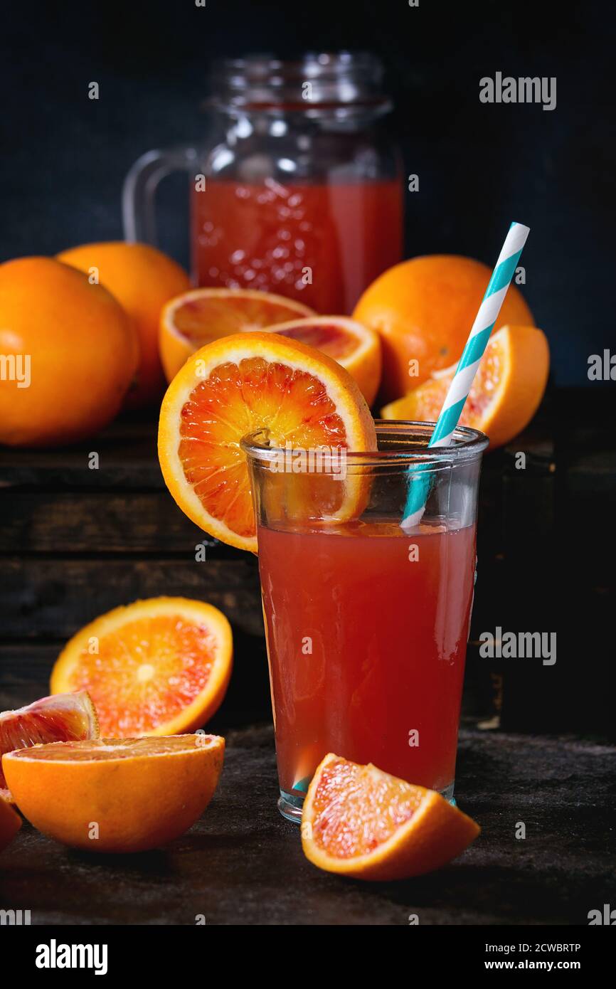 Affettato e tutto il sangue siciliano di arance e bicchiere di rosso fresco succo di arancia sopra il vecchio tavolo in legno. Scuro in stile rustico. Foto Stock