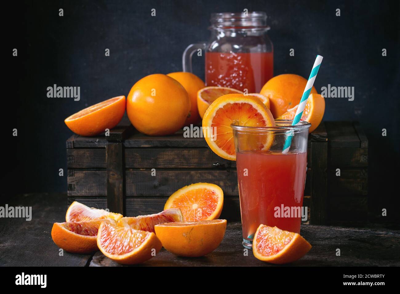 Affettato e tutto il sangue siciliano di arance e bicchiere di rosso fresco succo di arancia sopra il vecchio tavolo in legno. Scuro in stile rustico. Foto Stock