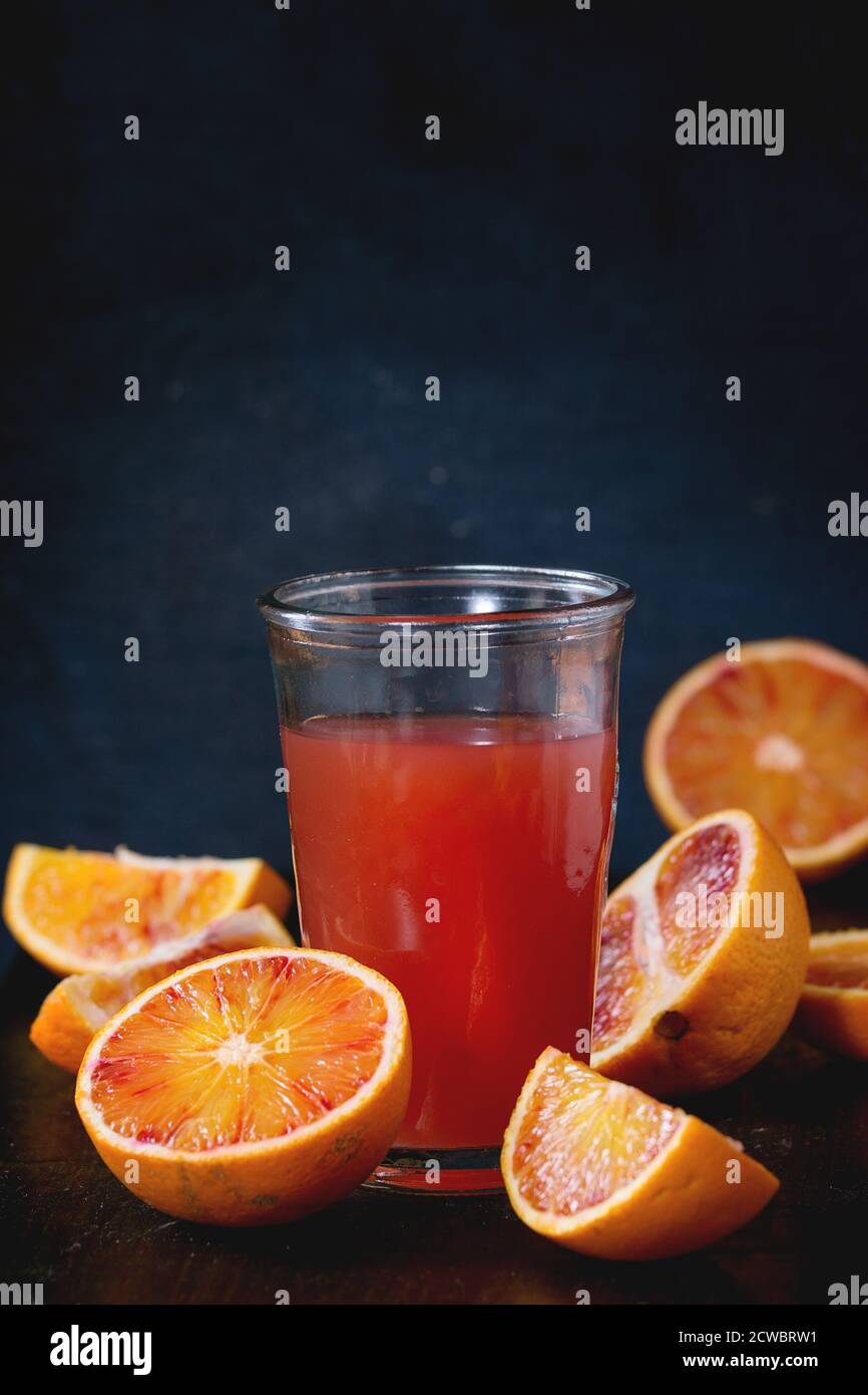 Fette di arance di sangue siciliano e un bicchiere di succo d'arancia rosso fresco sopra un vecchio tavolo di legno. Stile rustico scuro. Foto Stock