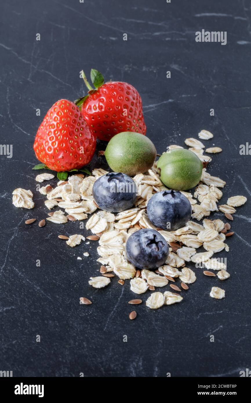 Fragole fresche, mirtilli, bacche kiwi e avena su marmo nero Foto Stock