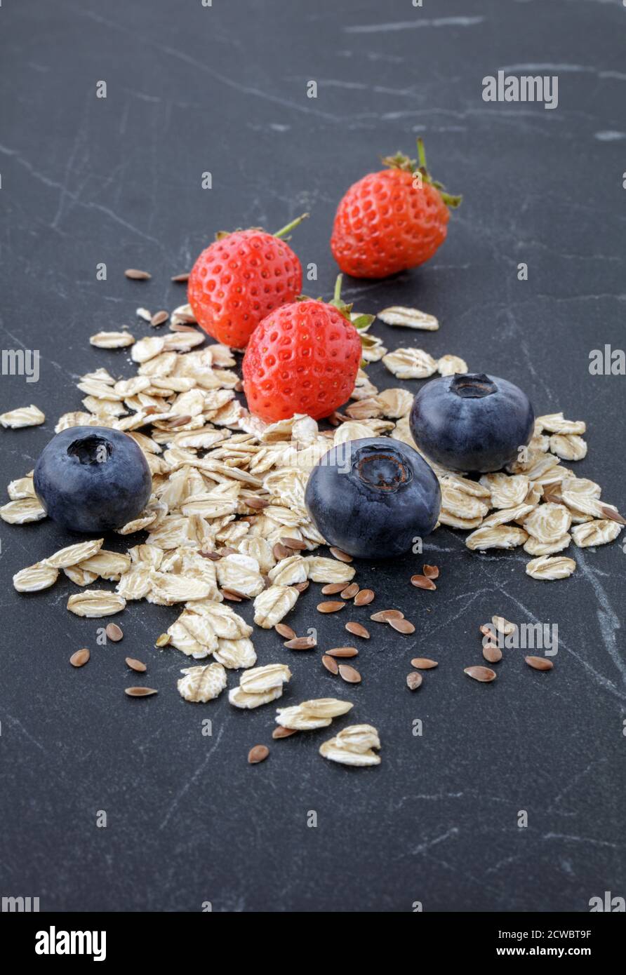 Mirtilli freschi, fragole con avena e semi di lino su marmo nero Foto Stock
