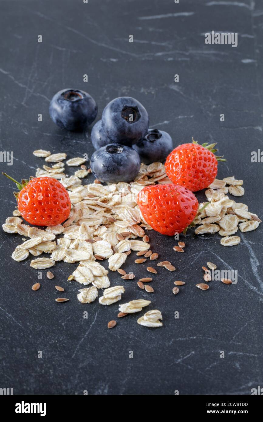 Fragole, mirtilli con avena e semi di lino su marmo nero Foto Stock