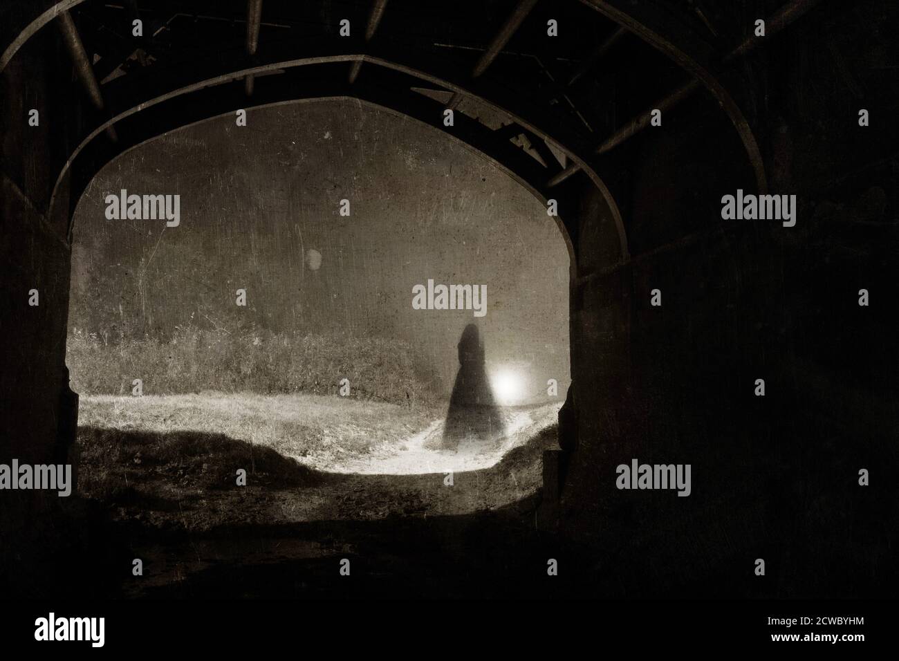 Il fantasma di una donna in un vestito in piedi in un tunnel, in una notte nebbiosa. Con un montaggio vintage, seppia, grunge. Foto Stock