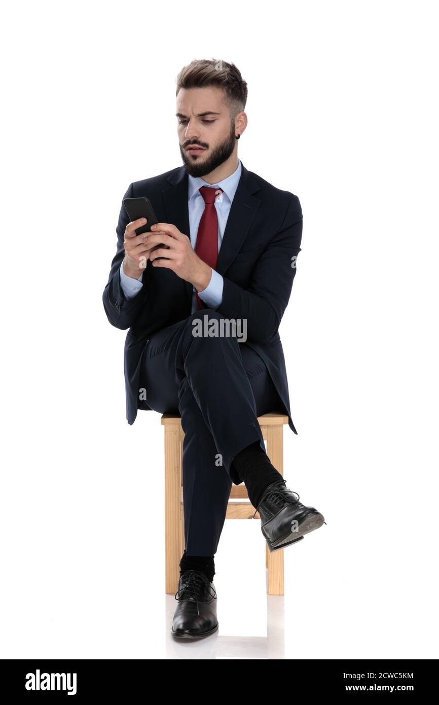 interessato giovane uomo d'affari che controlla e-mail e messaggi di testo sul cellulare, seduto isolato su sfondo bianco Foto Stock