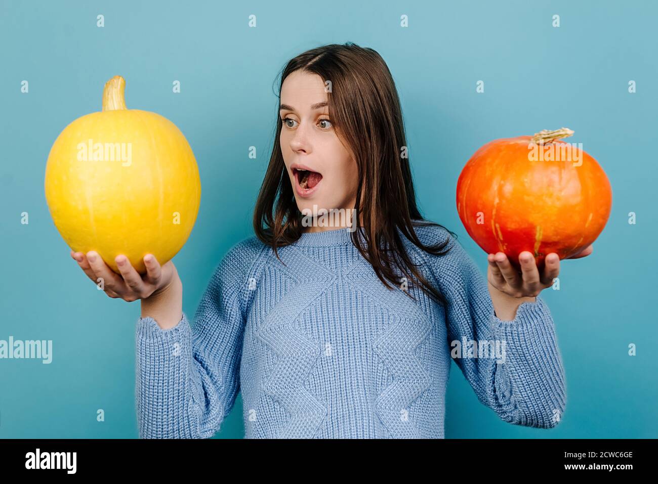 Colpo orizzontale di sorpresa impressionato giovane donna guarda sorprendentemente alla zucca arancione, trattiene il respiro dalla meraviglia Foto Stock
