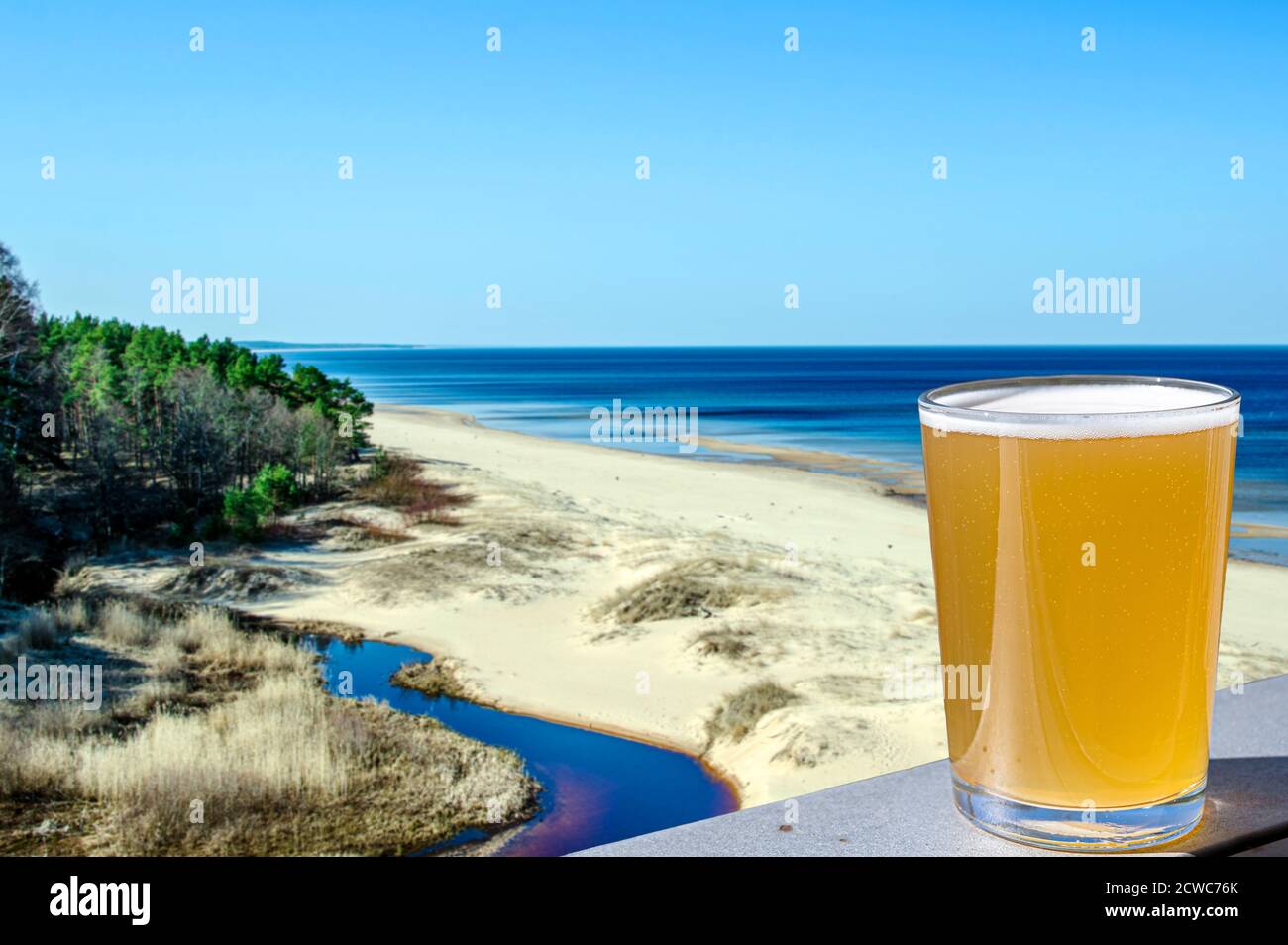 Bicchiere di birra leggera con vista sulla spiaggia di sabbia bianca e sul Mar Baltico in primavera, Lettonia. Foto Stock
