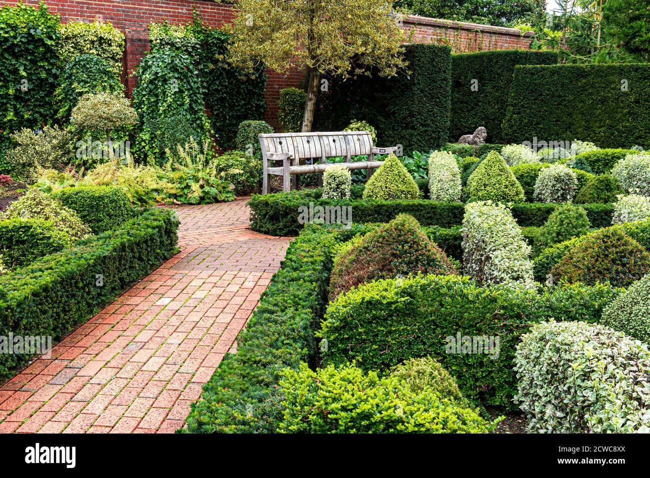 Il giardino del nodo parterre con la copertura della scatola con il percorso piastrellato, un attraente giardino curato e curato progettato murato con panca del giardino che ospita Surrey UK Foto Stock