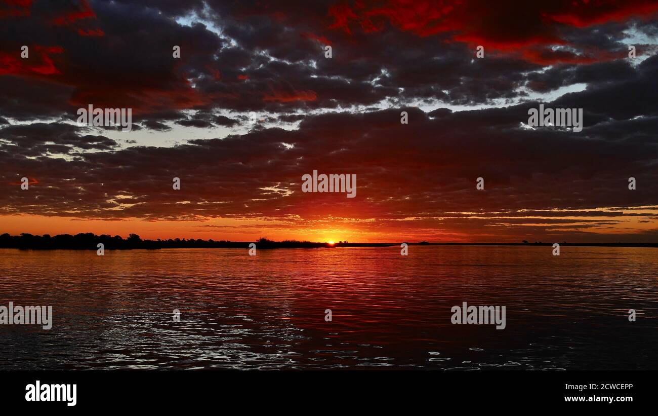 Incredibile tramonto multicolore con cielo rosso e arancione e nuvole che si riflettono in acqua sul fiume Chobe durante il safari in barca, il parco nazionale di Chobe, il Botswana. Foto Stock