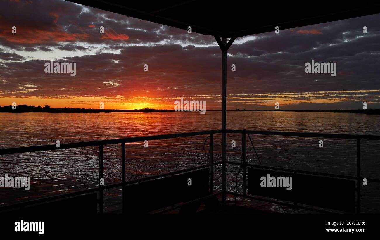 Incredibile tramonto colorato con cielo rosso e arancione che si riflette in acqua, girato da barca safari sul fiume Chobe vicino Kasane, Chobe Riverfront, Botswana. Foto Stock