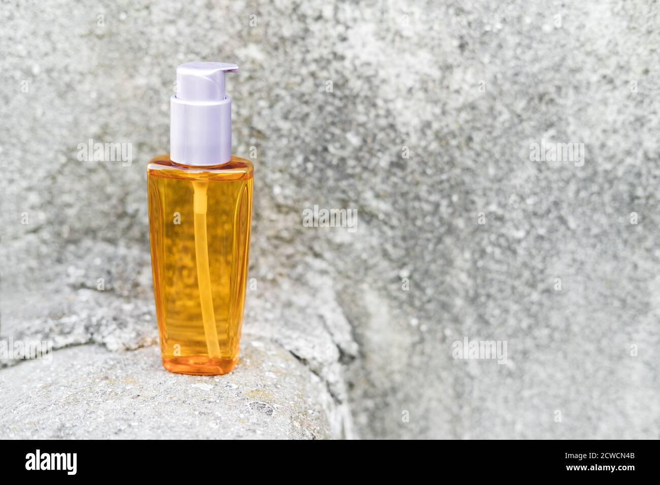 Una bottiglia d'olio arancione accanto a pietre naturali contro una parete grigia con luce naturale. Stile alla moda. Trucco cosmetico. CopySpace Foto Stock