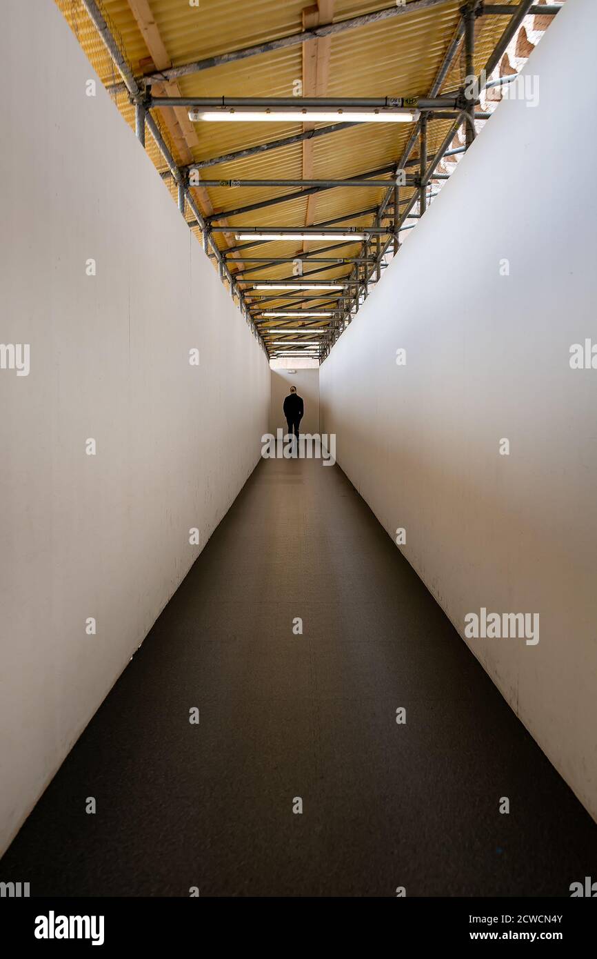 Uomo che cammina lungo un corridoio verso un'estremità ben illuminata esci Foto Stock