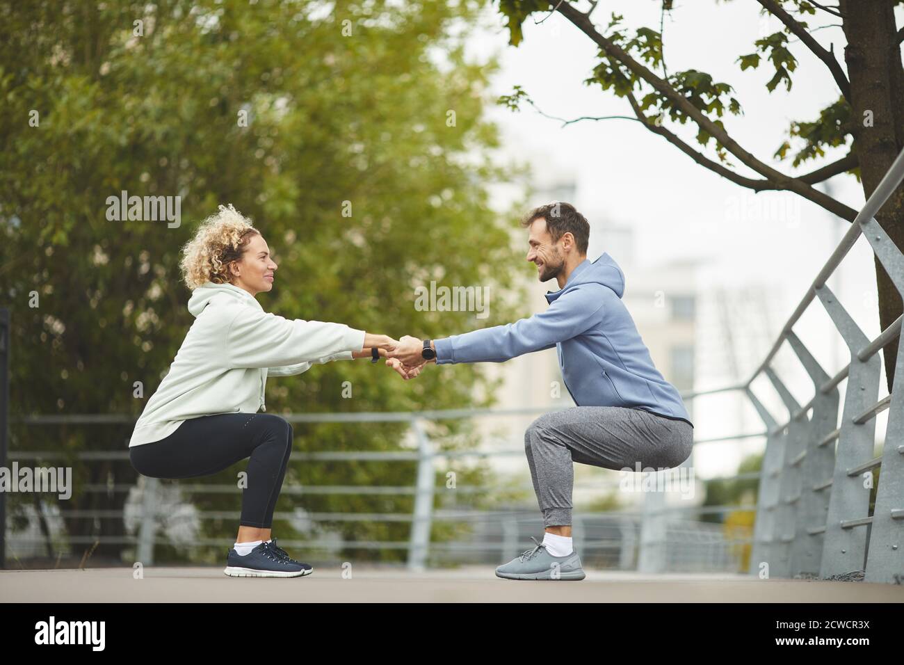 Giovane coppia sana che tiene le mani e si esercita durante l'addestramento dentro il parco Foto Stock
