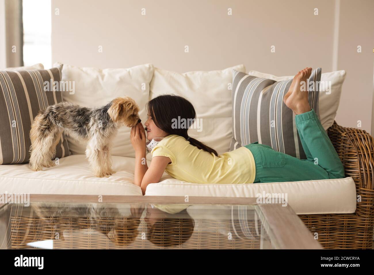 Caucasica ragazza passare il tempo a casa, indossare maschera, giocare con il suo cane. Distanza sociale durante il blocco della quarantena di Coronavirus Covid 19. Foto Stock