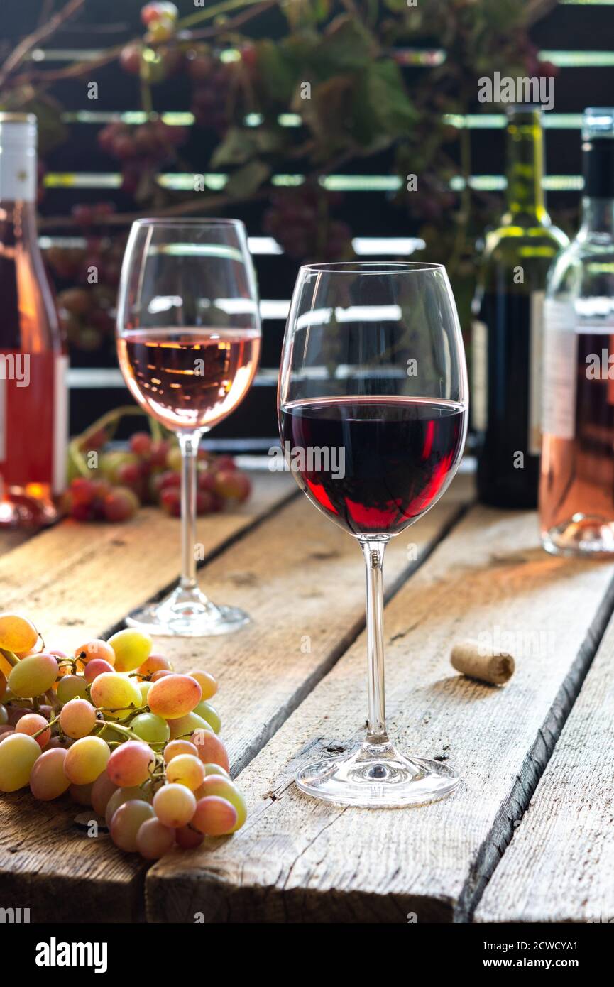 Bicchieri con vino rosso e rosa, ricreazione all'aperto, tavolo in legno con bicchieri di vino, bottiglie di vino e uva Foto Stock