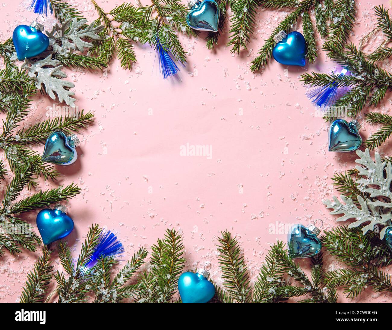 Ornamenti natalizi a forma di cuore blu con luci di festa a LED blu su sfondo rosa pastello, decorati con rami di abete. Bordo arrotondato, lotto di copia Foto Stock