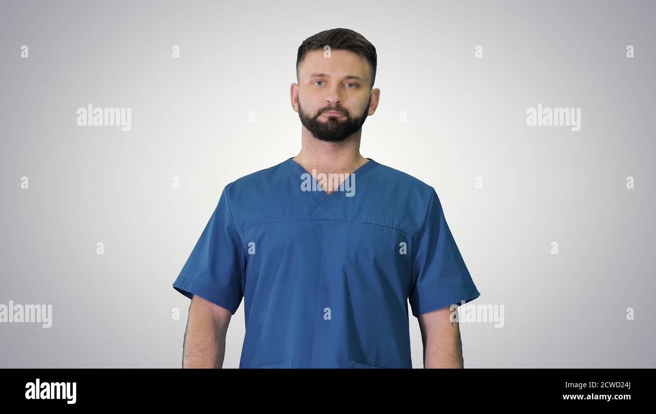 Chirurgo maschile serio con una barba che cammina su sfondo gradiente Foto Stock