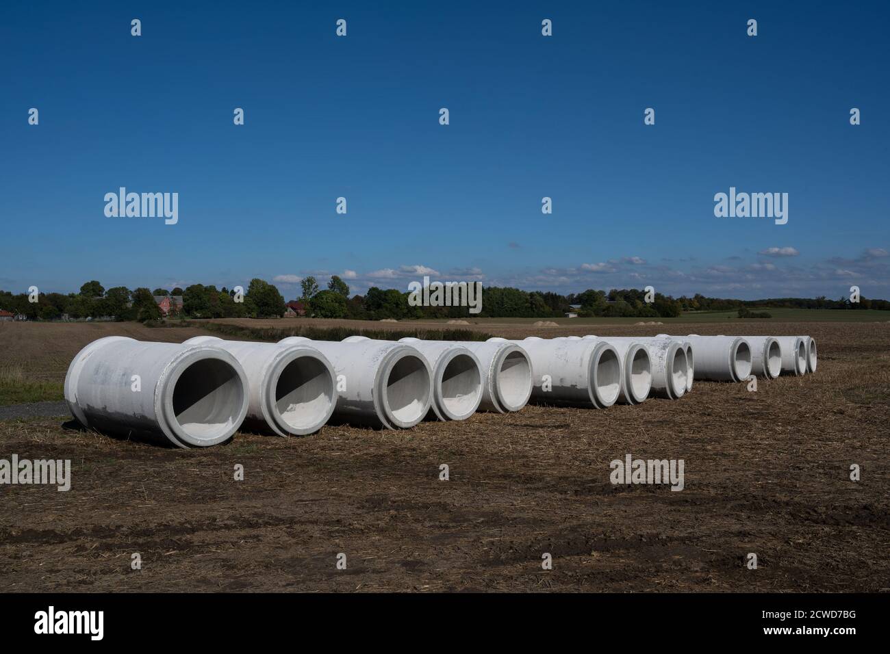 Grandi tubi d'acqua da cemento in una fila su un campo sotto un cielo blu, cantiere per un sistema fognario di drenaggio contro l'allagamento, copia spazio, sel Foto Stock