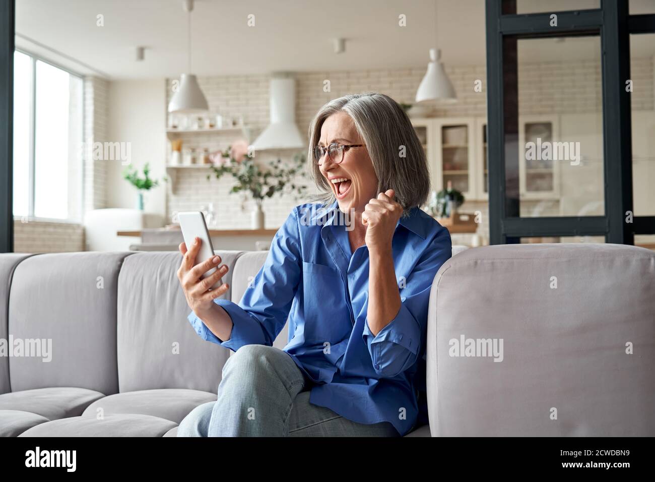 Entusiasta anziana vincitrice del messaggio di lettura sullo smartphone a casa. Foto Stock