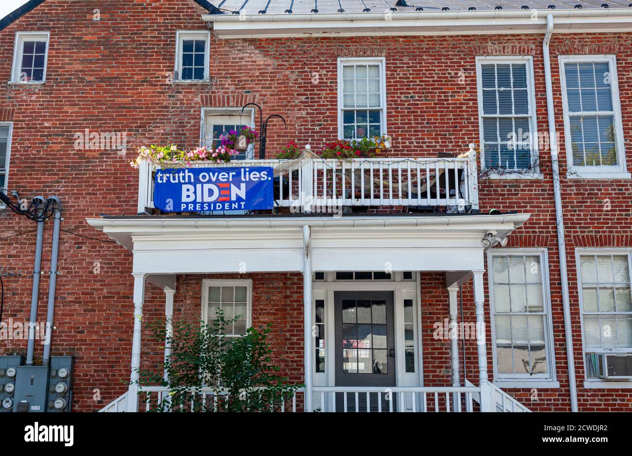 Berryville, VA, USA 09/27/2020: Un Biden blu per la bandiera del presidente è attaccato alle ringhiere di legno del balcone del secondo piano ad un ho di mattone vintage Foto Stock
