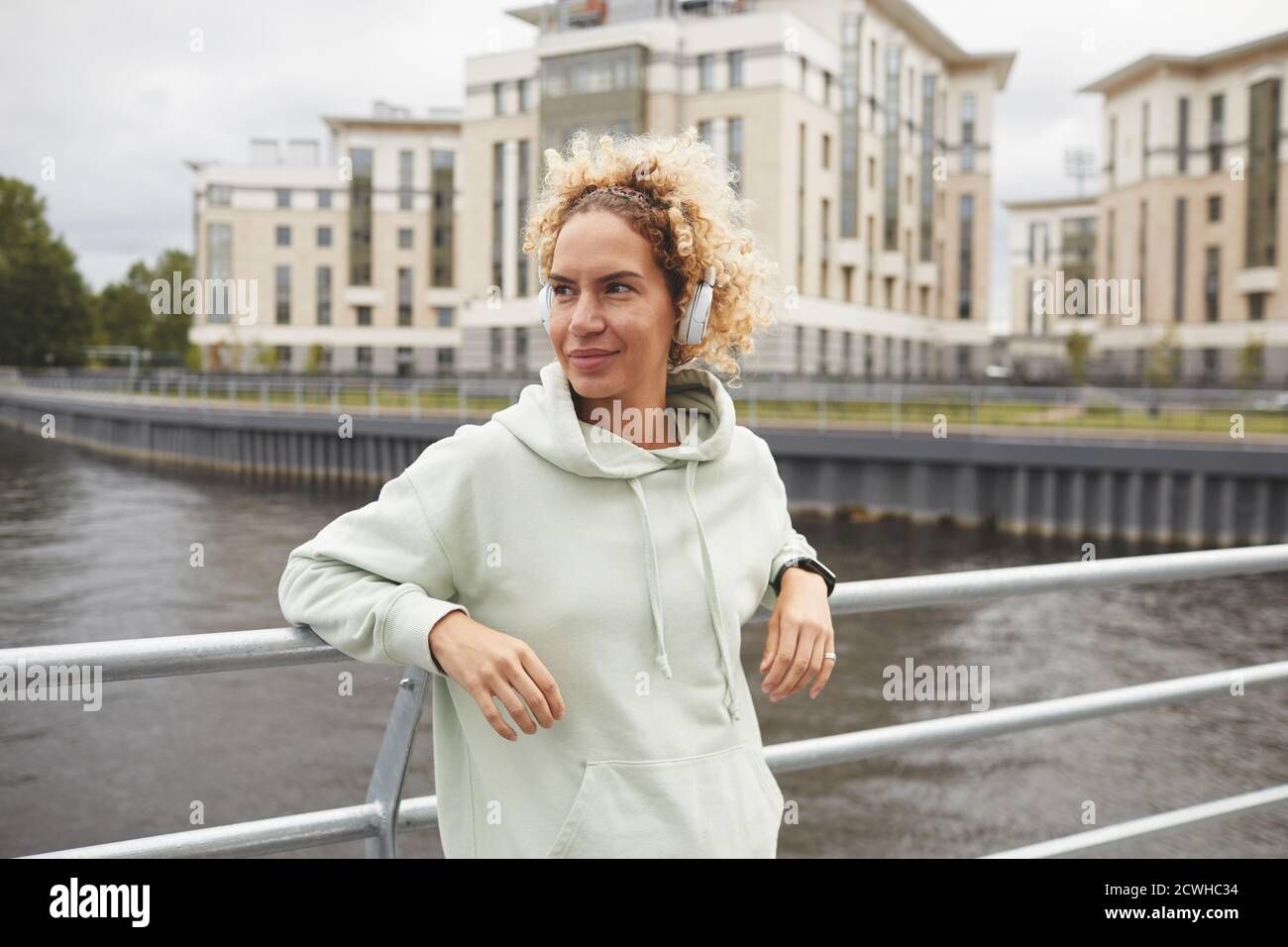 Giovane donna in cuffia in piedi sul ponte nel città e godersi la musica Foto Stock