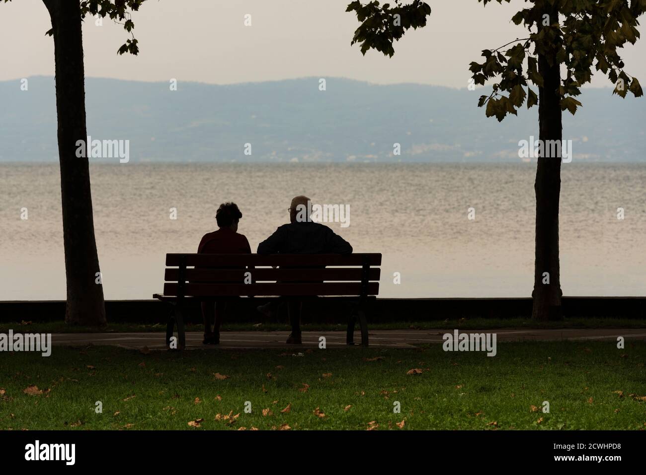 Un paio di anziani guarda il paesaggio seduto su una panchina al tramonto Foto Stock