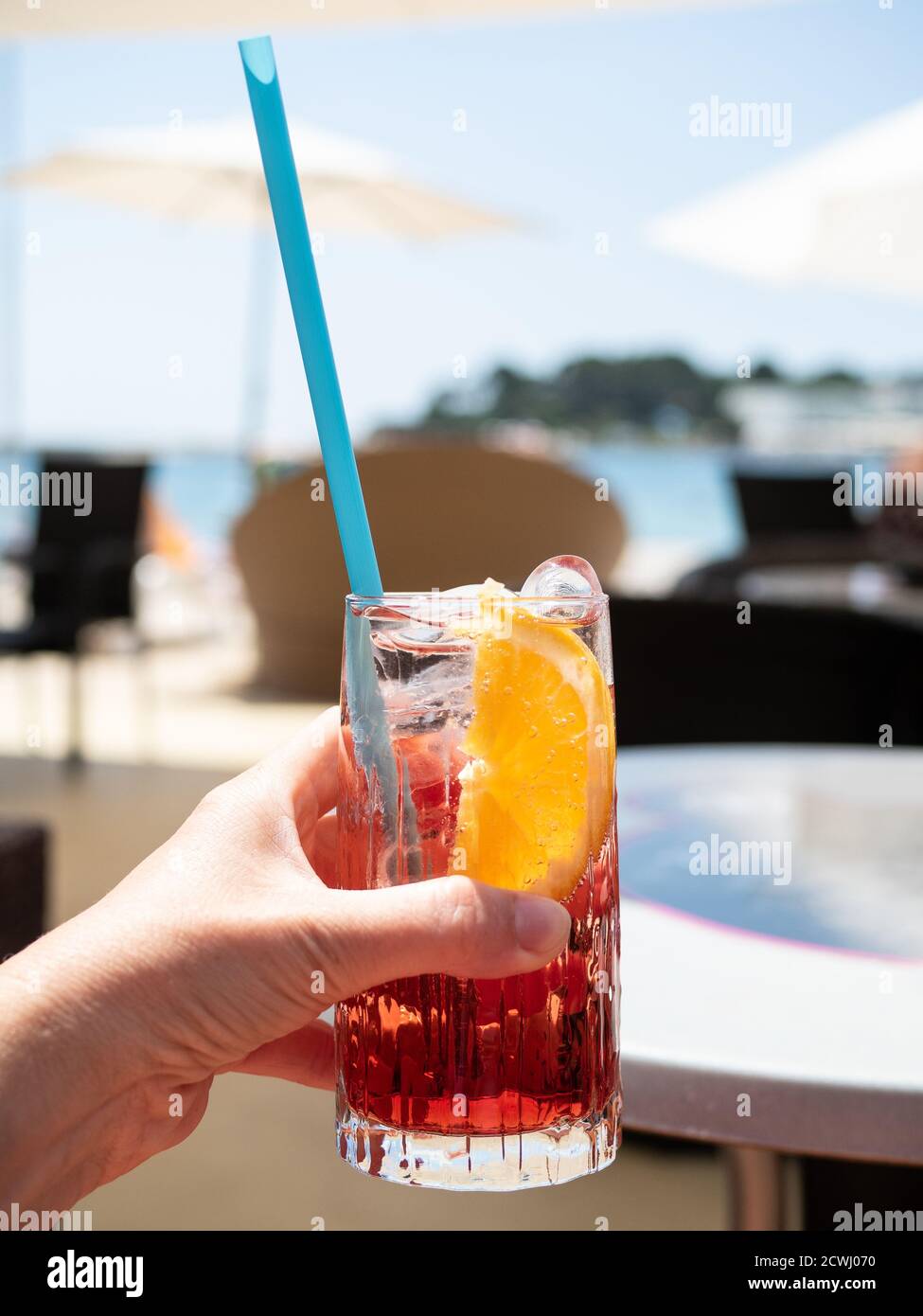 Vetro femmina di campari con soda e cannuccia di plastica. Spiaggia con ombrelloni in giornata di sole. Foto Stock
